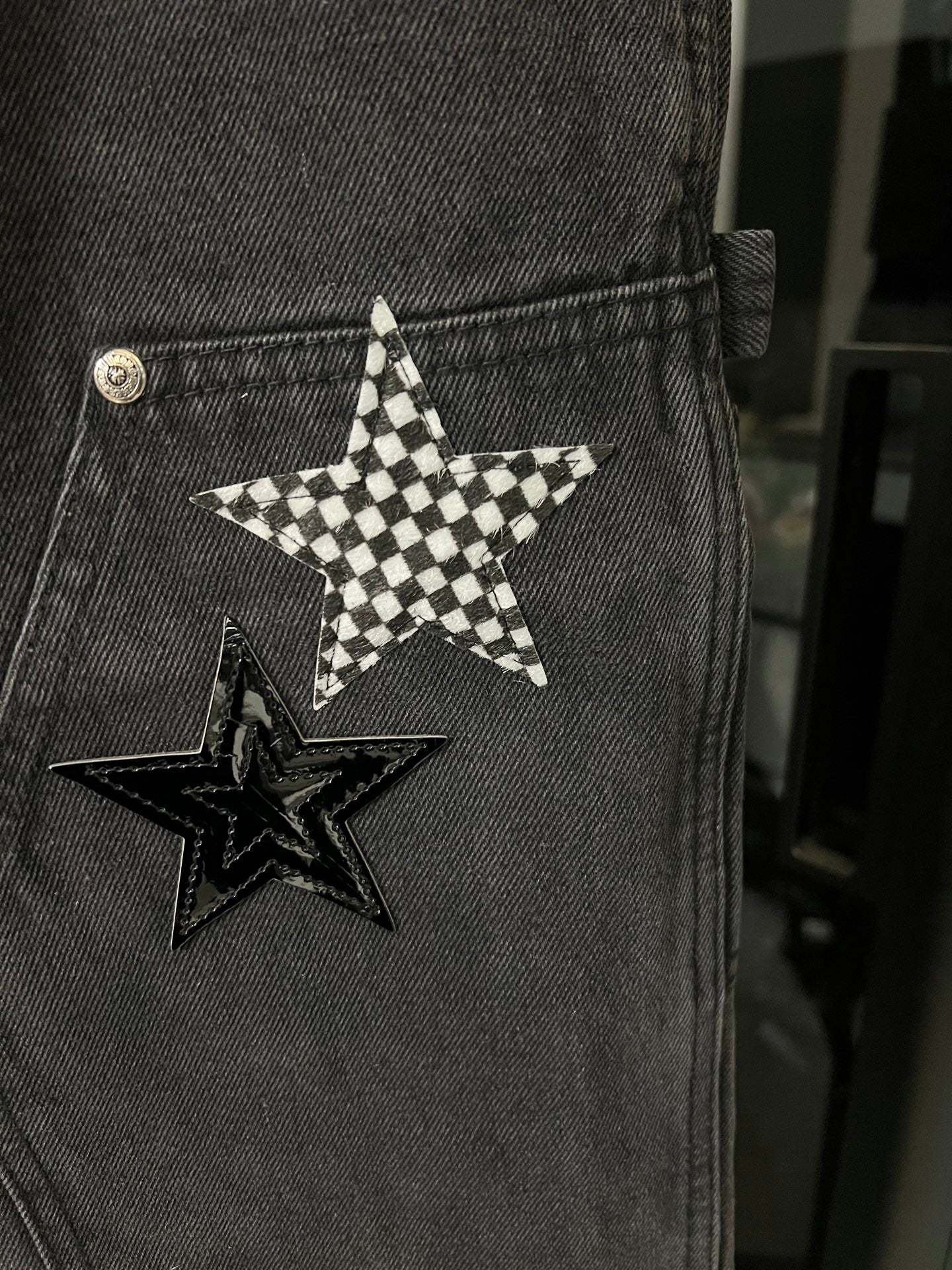 Dark gray denim pants pocket with checkered star patch and metal button