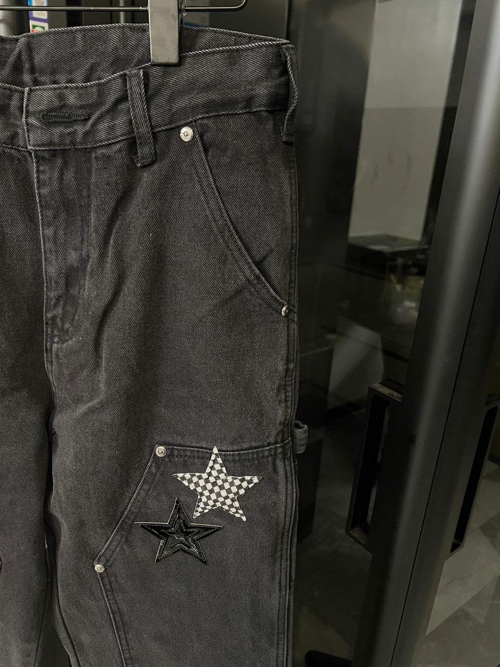 Dark gray denim pants close-up with star patch on front pocket area