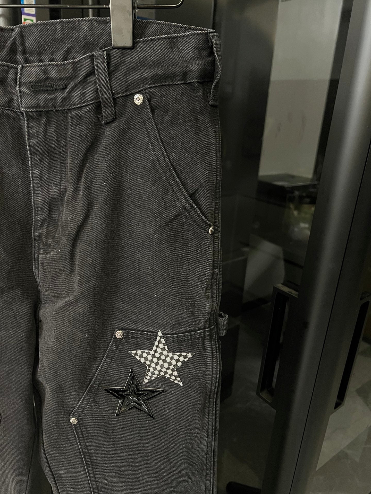 Dark gray denim pants close-up with star patch on front pocket area