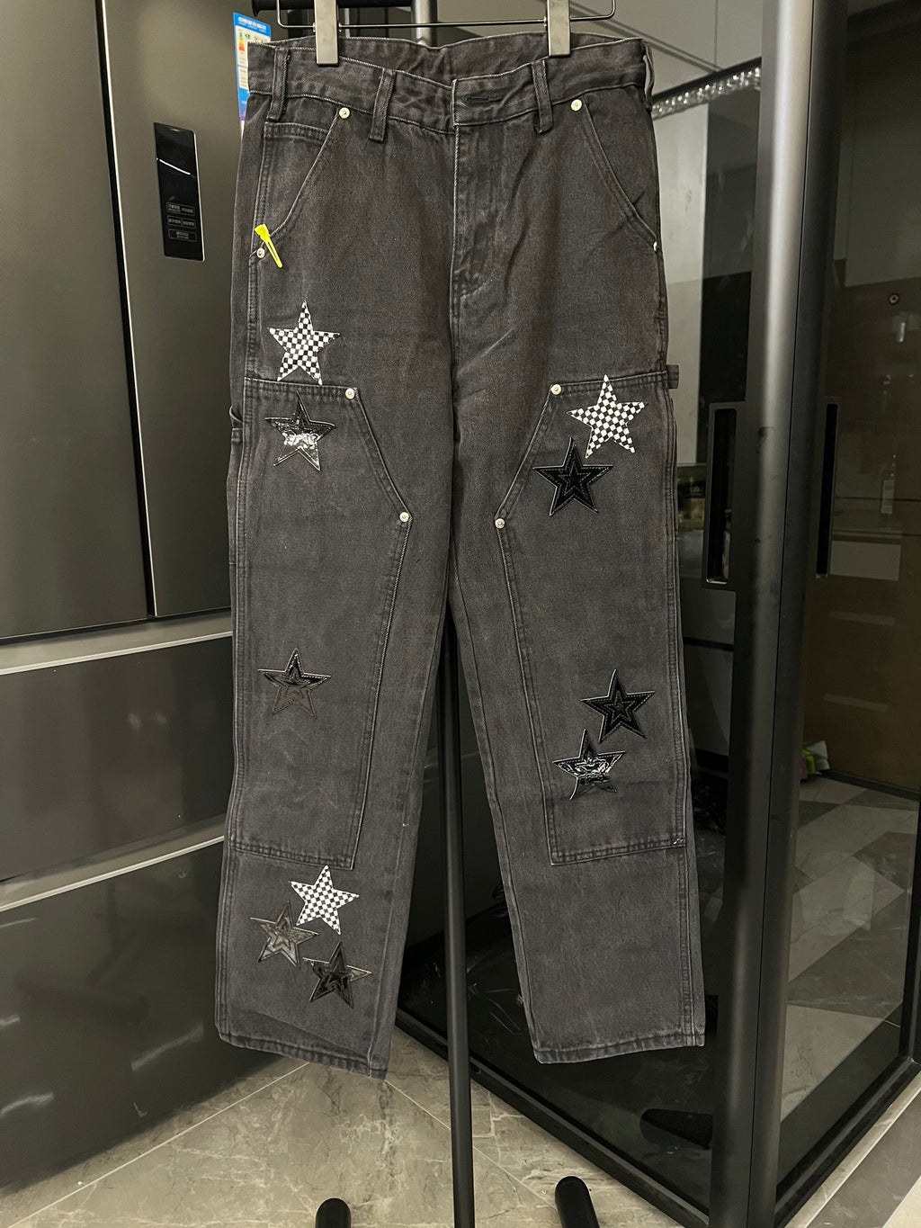 Dark gray denim pants with distressed finish and stitched star patches on legs