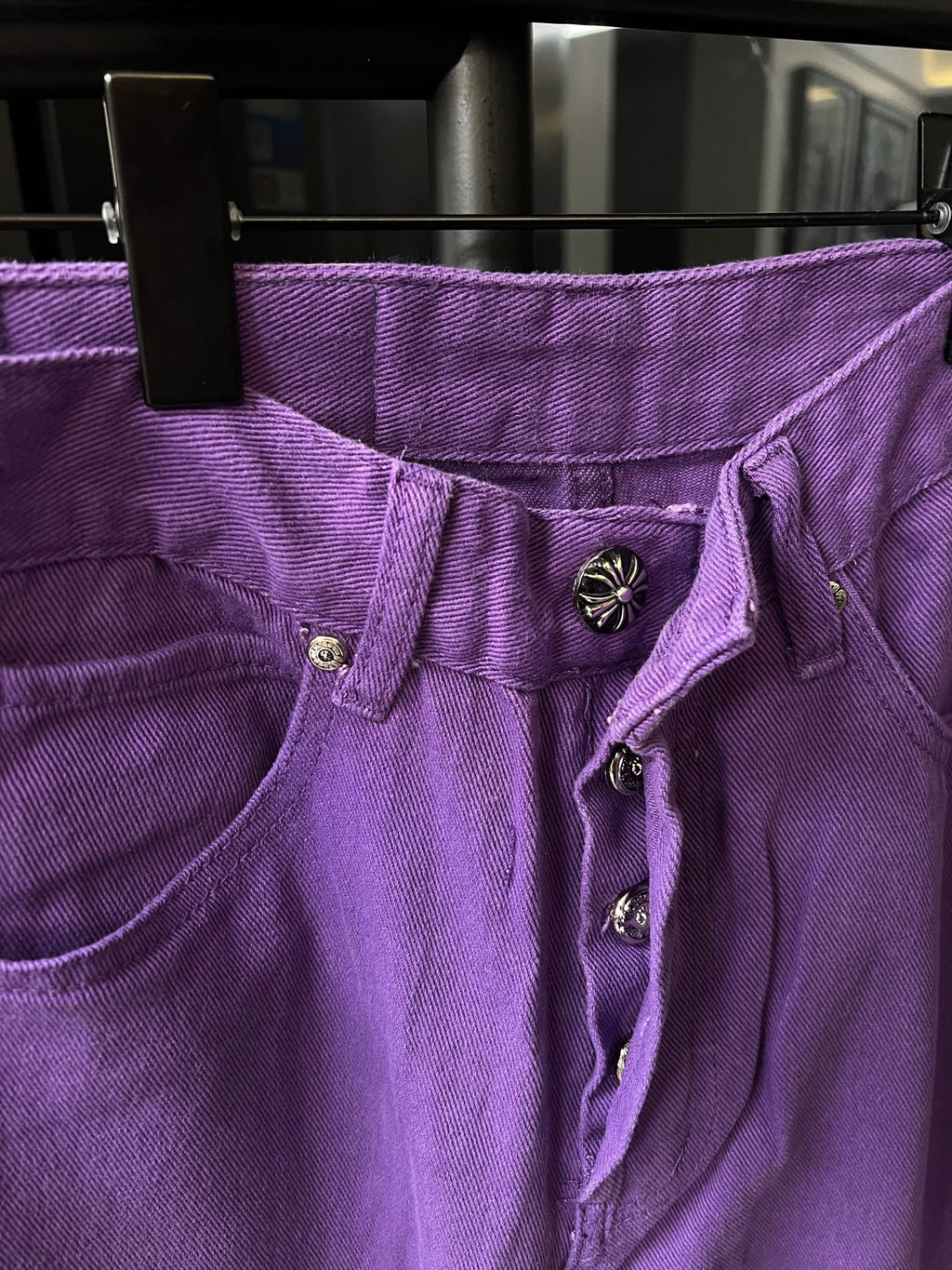 Purple pants waistband close-up with button placket and embroidered emblem