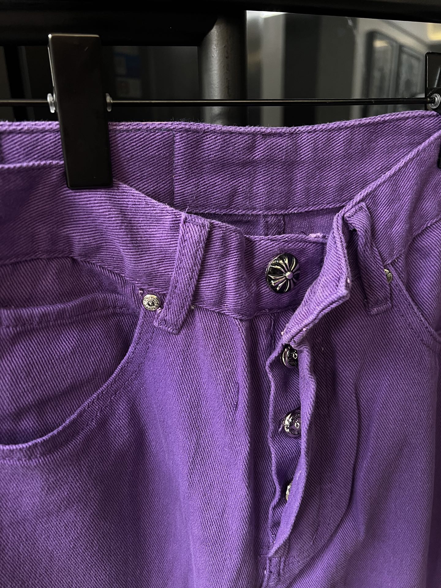 Purple pants waistband close-up with button placket and embroidered emblem