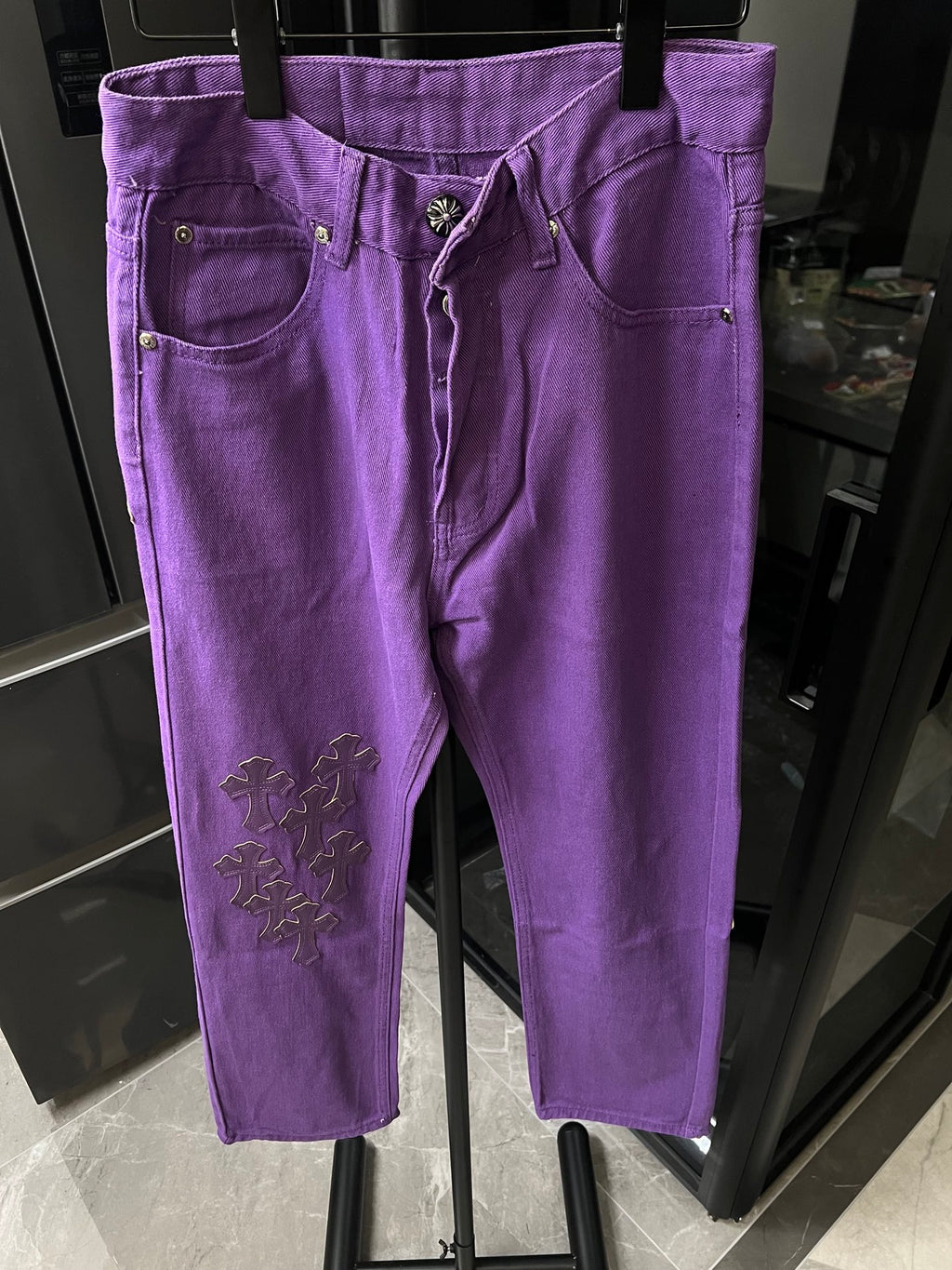 Purple denim pants with button fly and belt loops, embroidered cross patch at knee