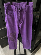 Purple denim pants with button fly and belt loops, embroidered cross patch at knee
