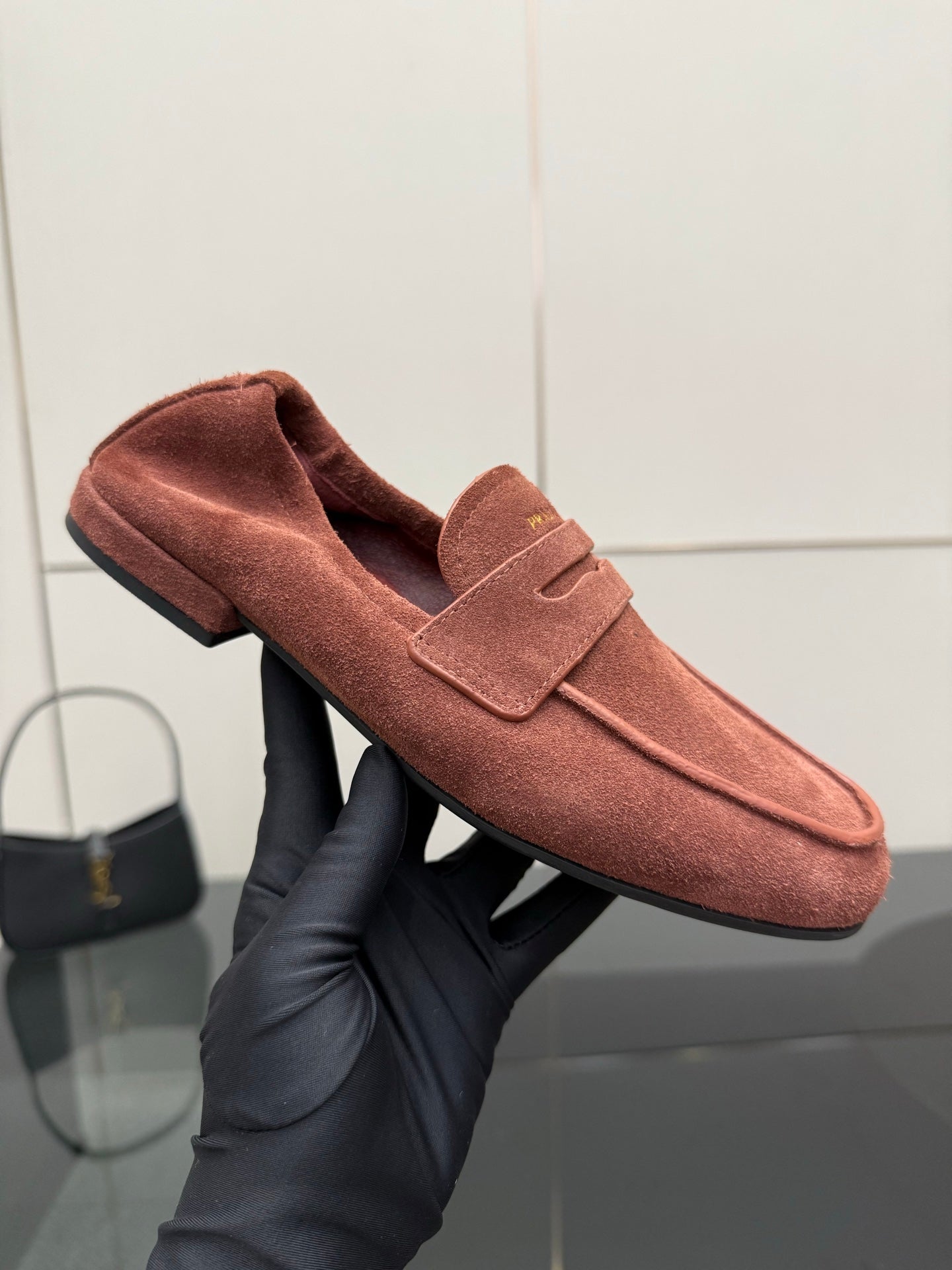 Prada rust-brown suede loafer held in hand, showing strap and upper