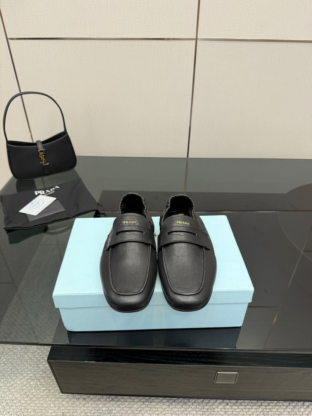 Black leather loafer with front strap, gold logo detail, flat sole