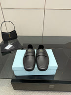 Black leather loafer with front strap, gold logo detail, flat sole