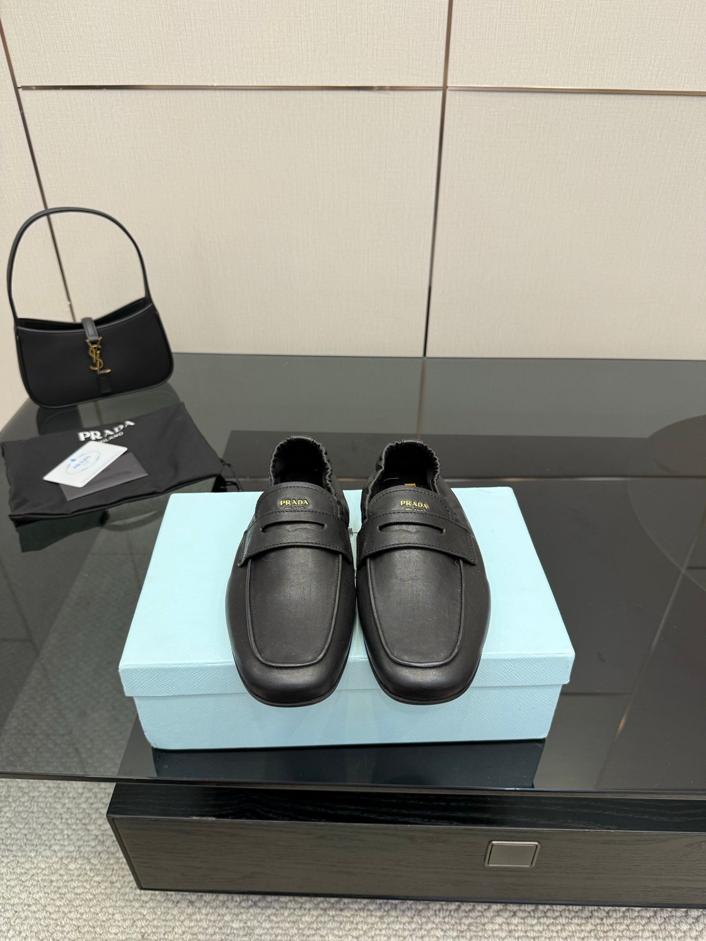 Black leather loafer with front strap, gold logo detail, flat sole