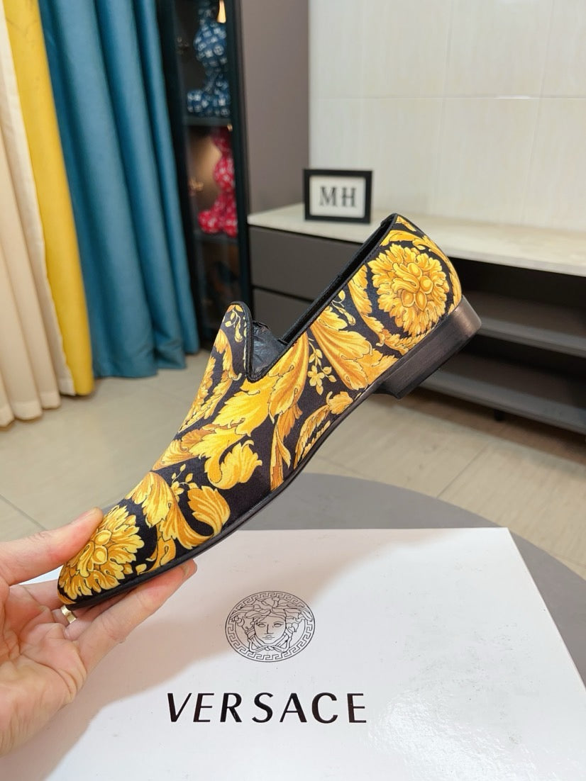 Slip-on loafer held in hand, dark fabric with yellow floral pattern and black collar.