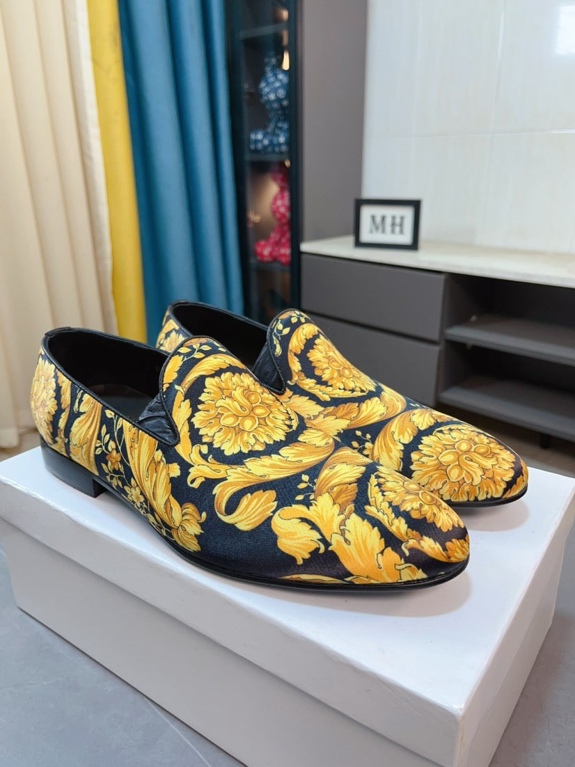Pair of floral slip-on loafers, dark base with yellow ornate prints.