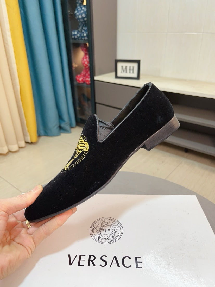 Black velvet loafer with gold Medusa emblem, held up for view