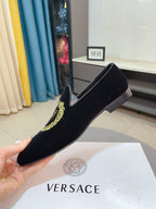 Black velvet loafer with gold embroidered crest, held in hand