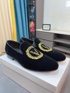 Pair of black velvet loafers with gold embroidered crest, side view