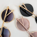Multiple round sunglasses with gold-tone and pastel frames, mirrored lenses, on display.