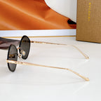 Round sunglasses with black lenses and gold-tone frame, side view of metal temple arms.