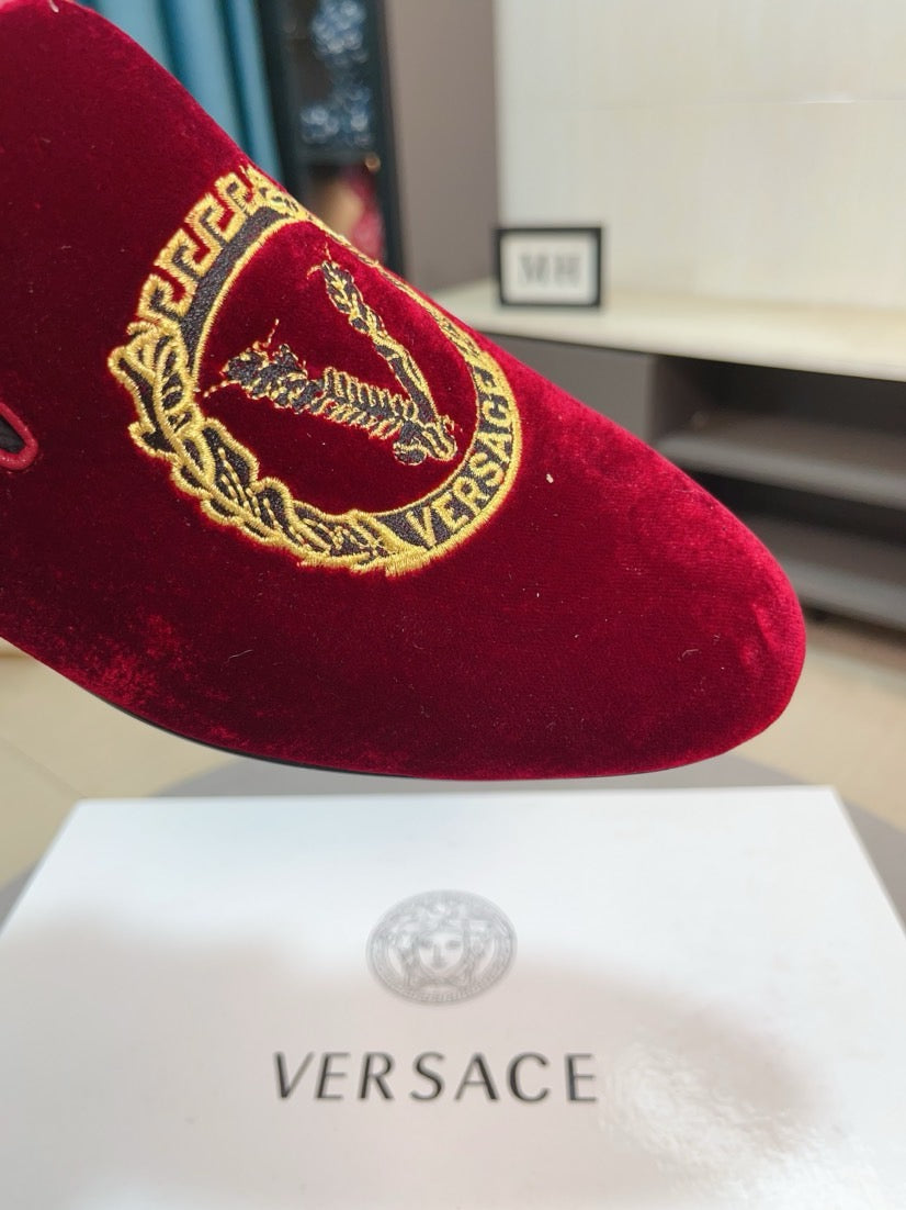 Close-up of a burgundy velvet loafer with ornate gold crest embroidery on the vamp
