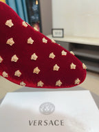 Close-up of deep red velvet loafer with gold stud embellishments on the top.