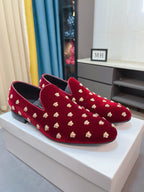 Pair of deep red velvet loafers with gold stud accents and low heel profile.