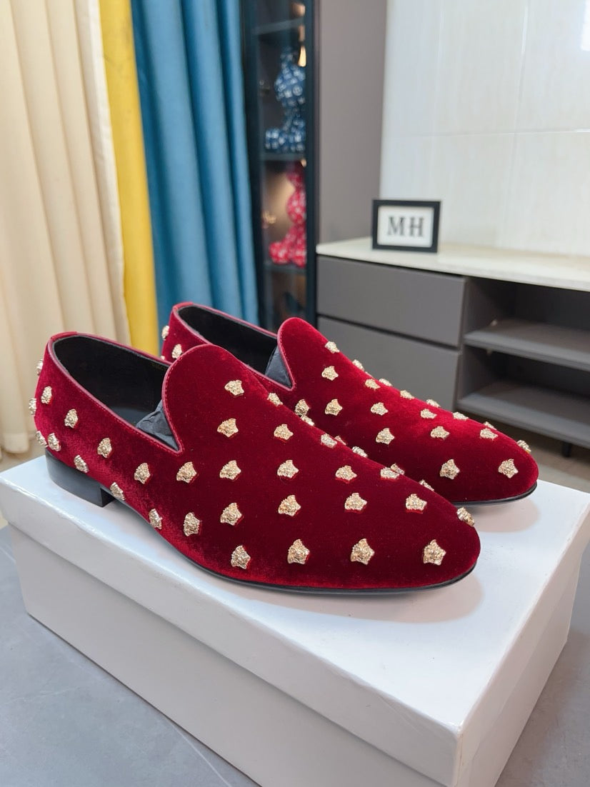 Pair of deep red velvet loafers with gold stud accents and low heel profile.