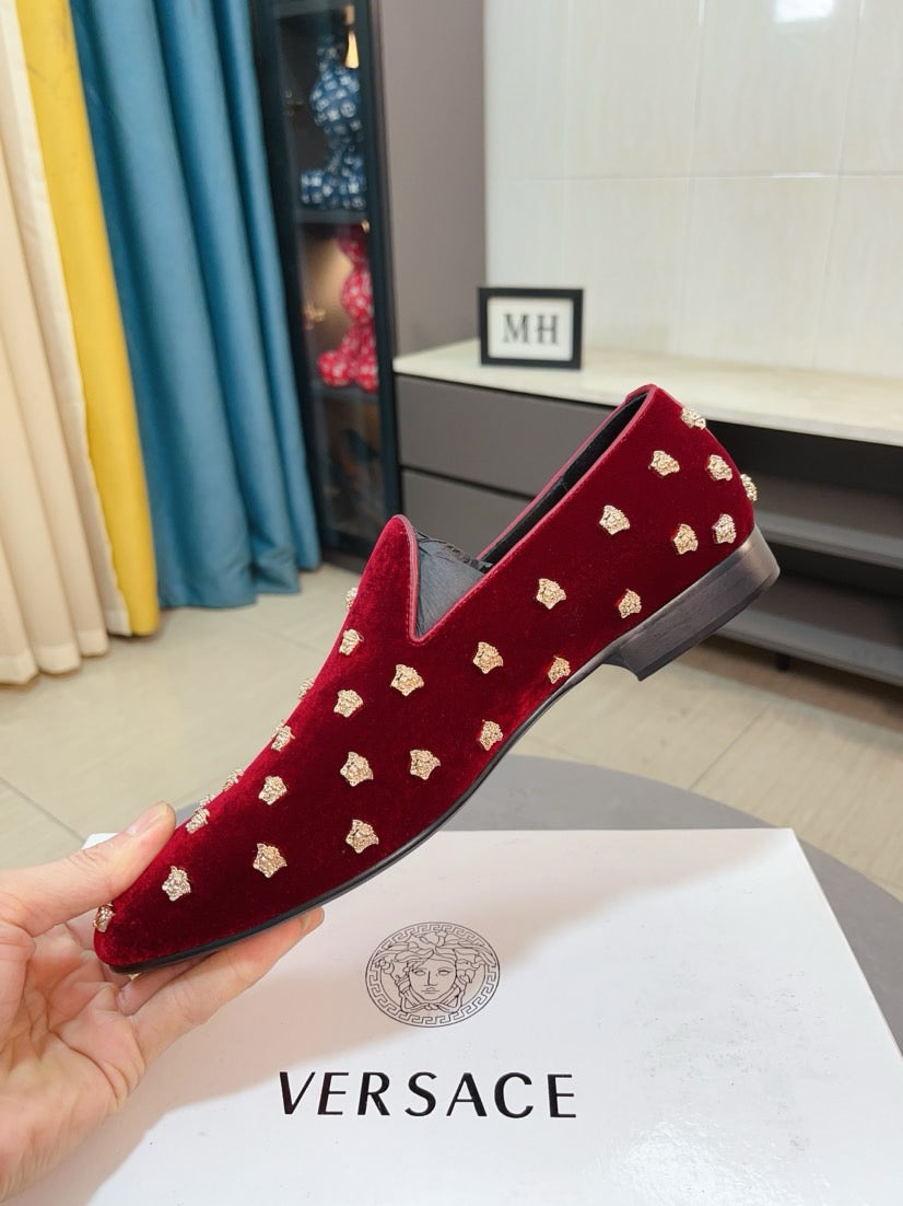 Hand holding red velvet loafer with repeating gold stud pattern and cushioned vamp.