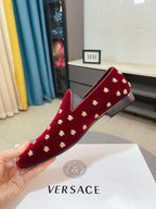 Hand holding red velvet loafer with repeating gold stud pattern and cushioned vamp.