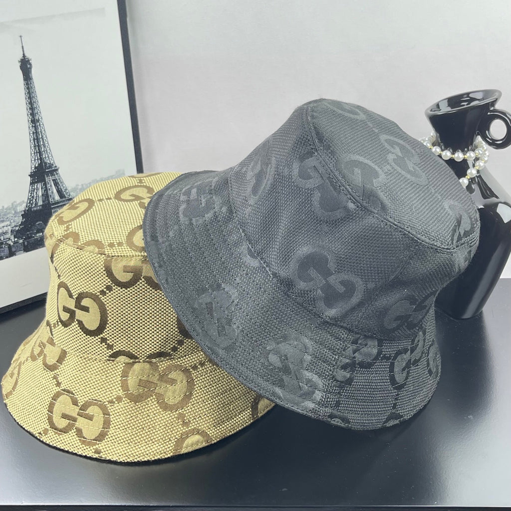 Gucci GG monogram bucket hat in dark gray canvas with wide brim, next to beige cap