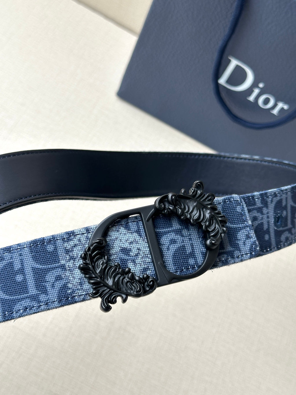 Blue monogram belt with black adjustable buckle and detailed medallion clasp.