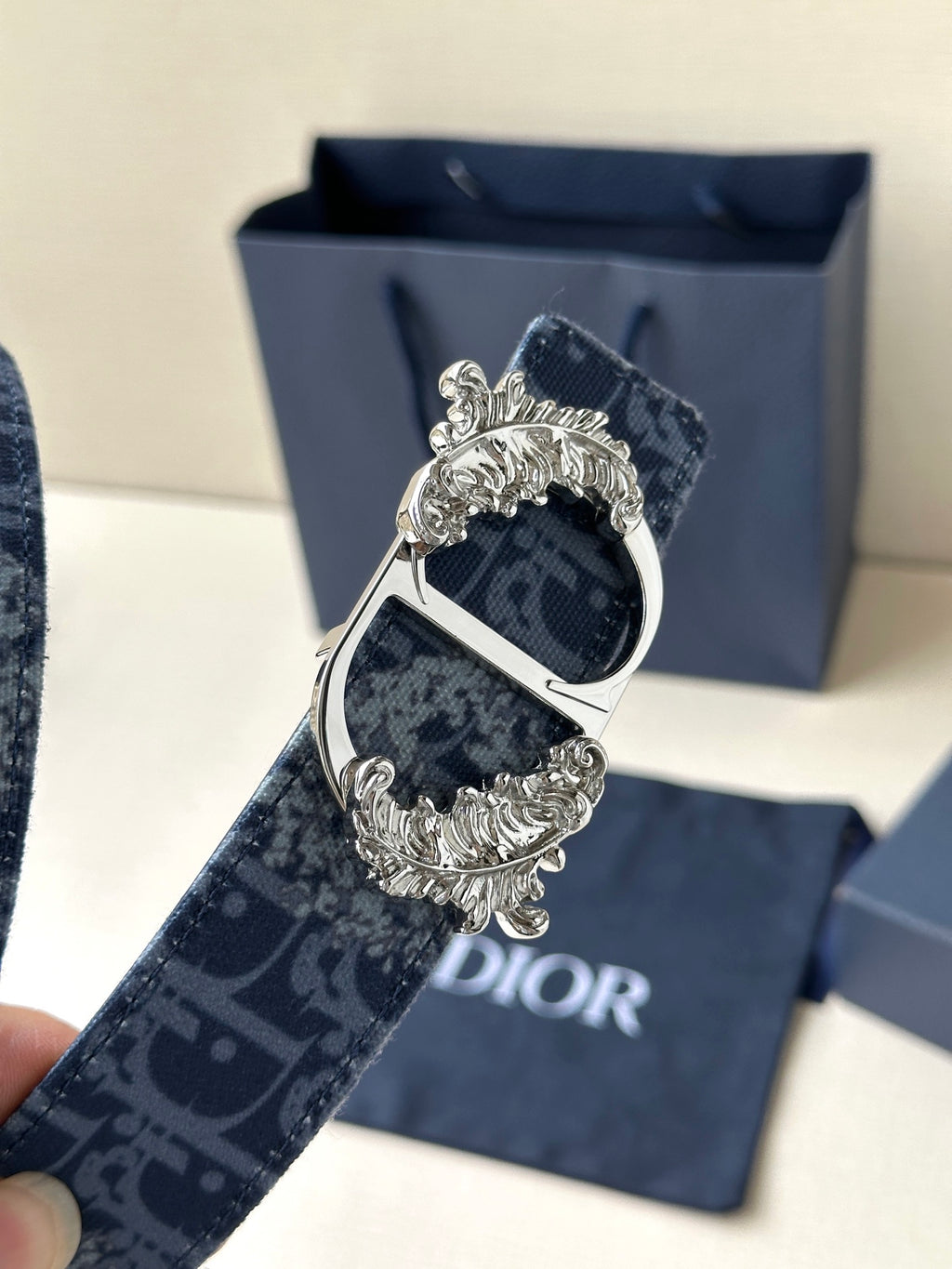 Dior belt buckle close-up: dark blue monogram strap with silver-toned ornate frame