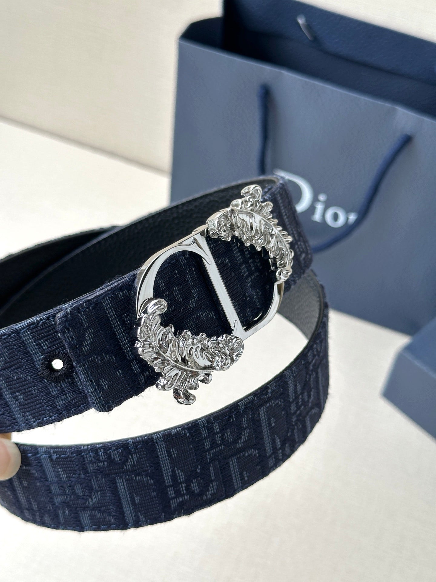 Dark blue Dior belt close-up showing silver buckle, oval center, and decorative scrolls