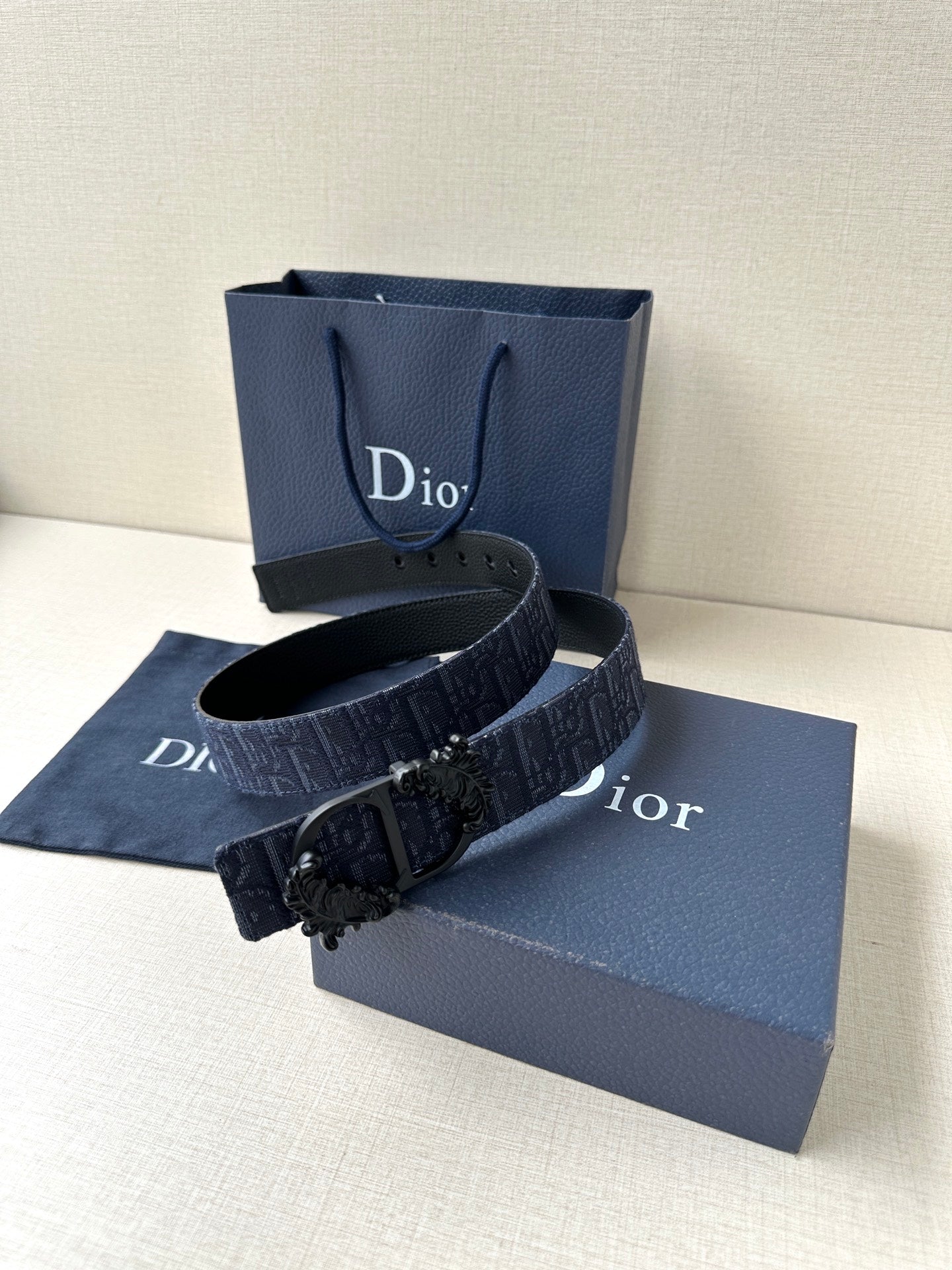 Dior belt coiled on display: dark blue strap with black ornate buckle and keeper