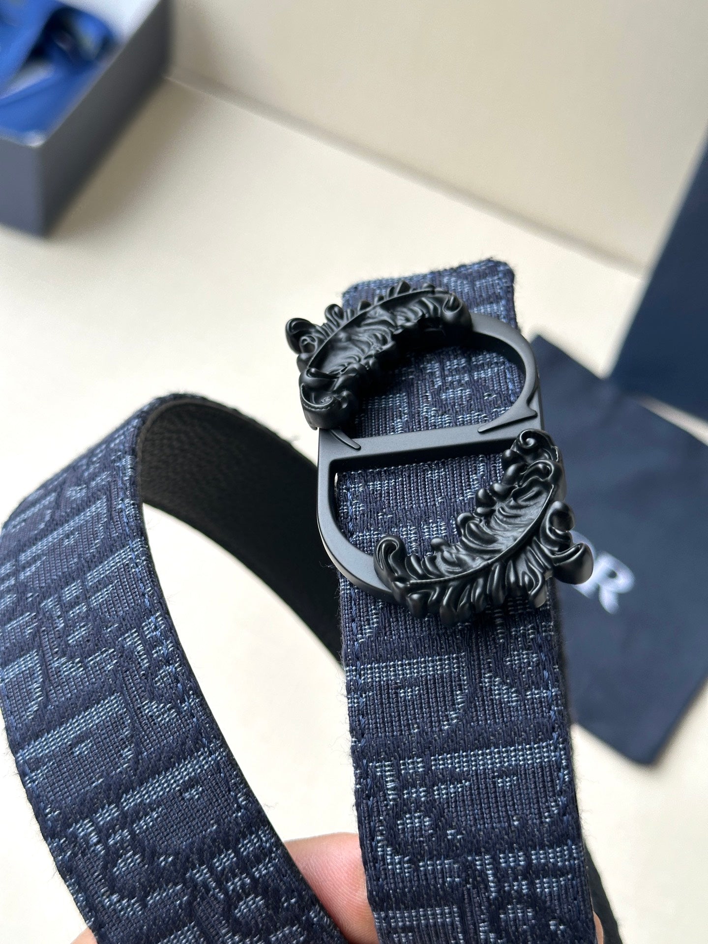 Dior belt buckle close-up on dark blue strap with textured black centerpiece