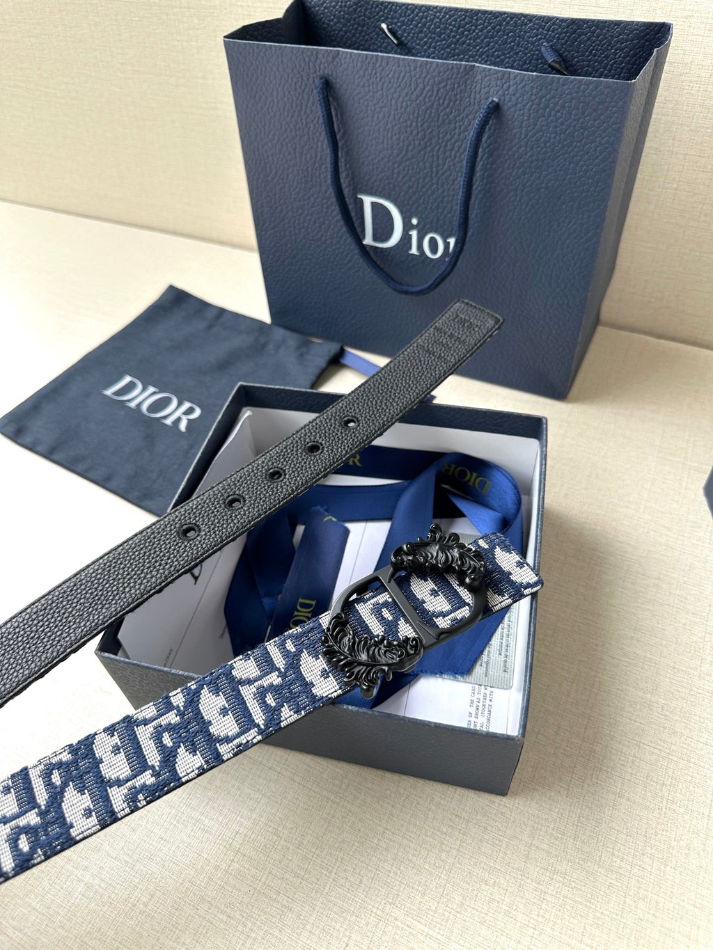 Dior belt laid flat with blue monogram band, black leather holes, and buckle