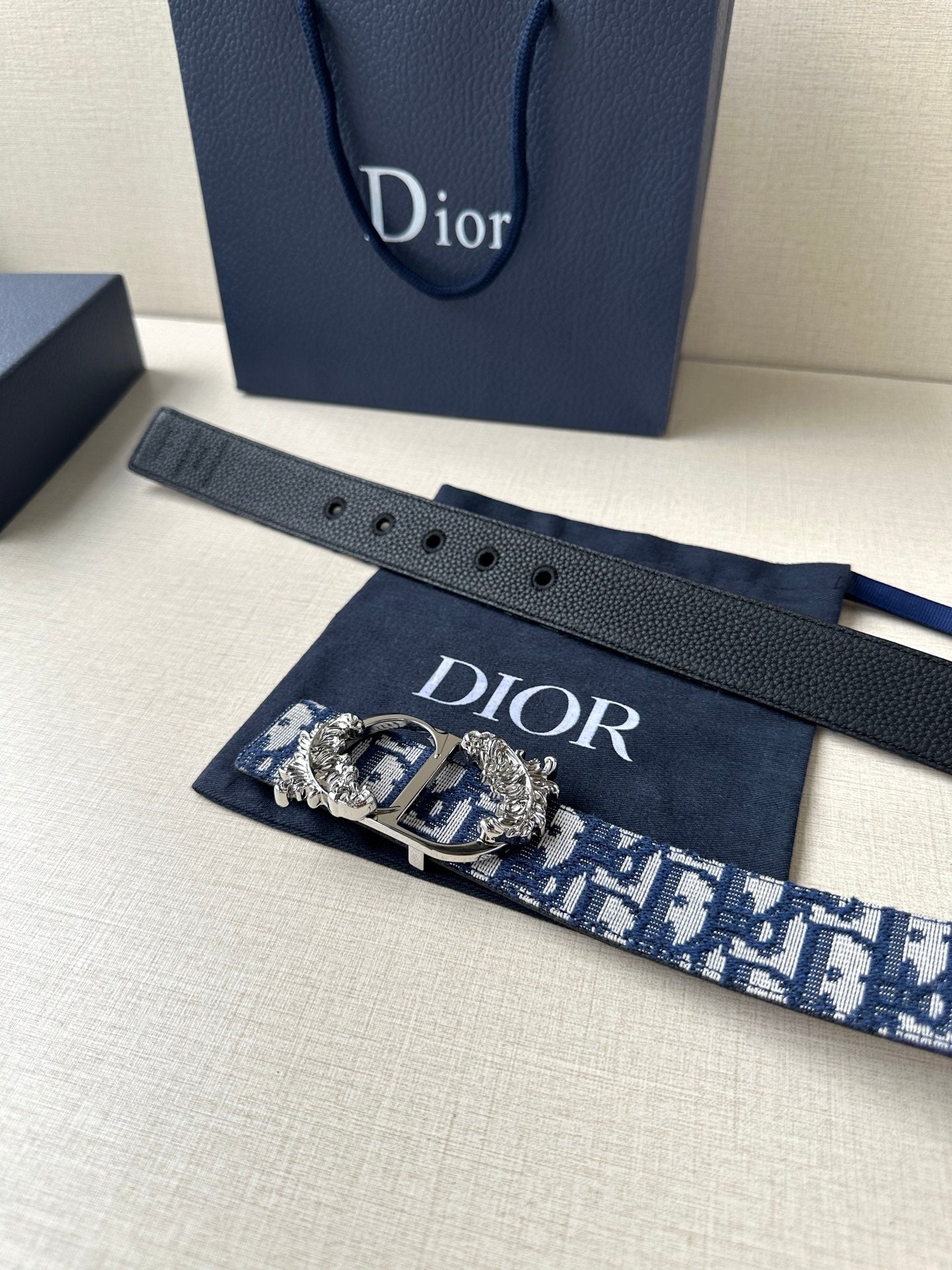 Dior belt with navy and light blue logo strap, gold buckle, and pin holes