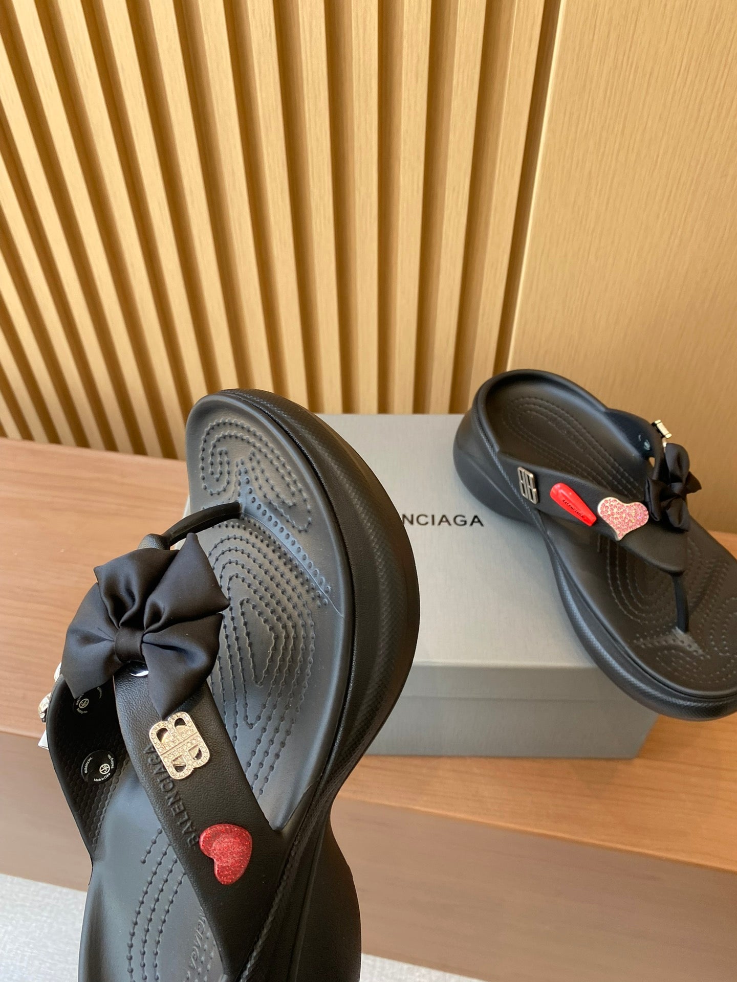 Black sandals with textured strap and heart charm, angled view of footbed