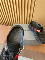 Black sandals with heart charm and bow detail, close-up of thong strap