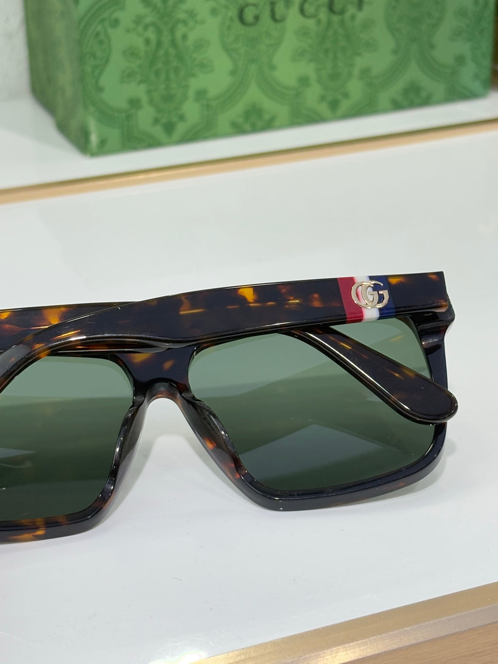 Gucci sunglasses close-up with tortoise frames and green lenses, colorful logo on top bar