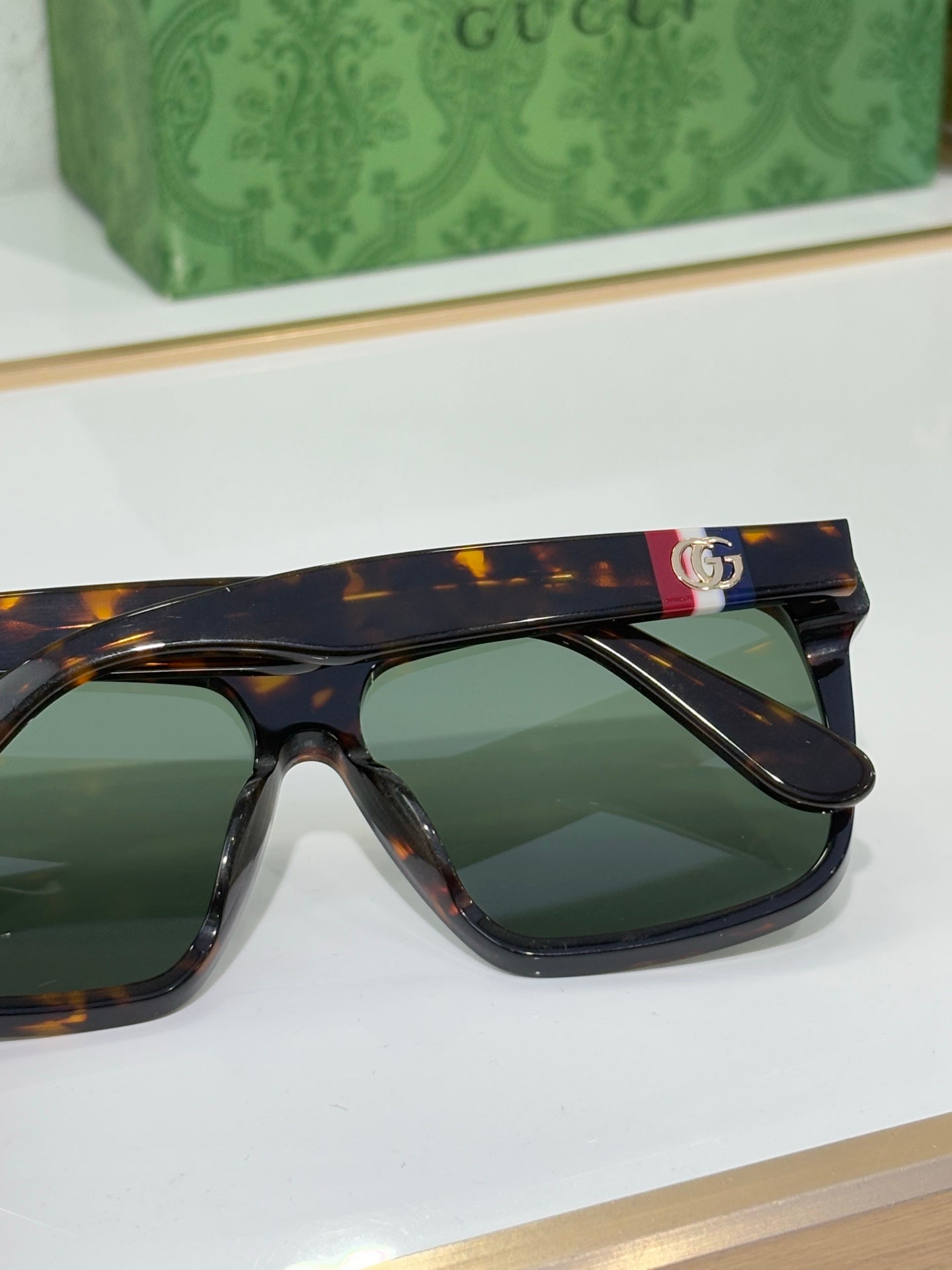 Gucci sunglasses close-up with tortoise frames and green lenses, colorful logo on top bar
