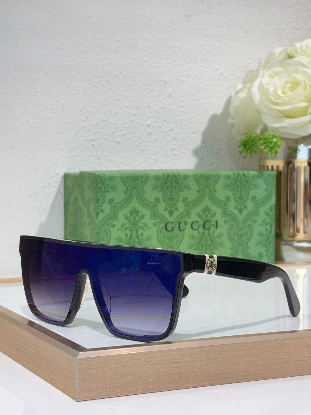 Gucci sunglasses with dark frames and blue lenses, gold logo on temple