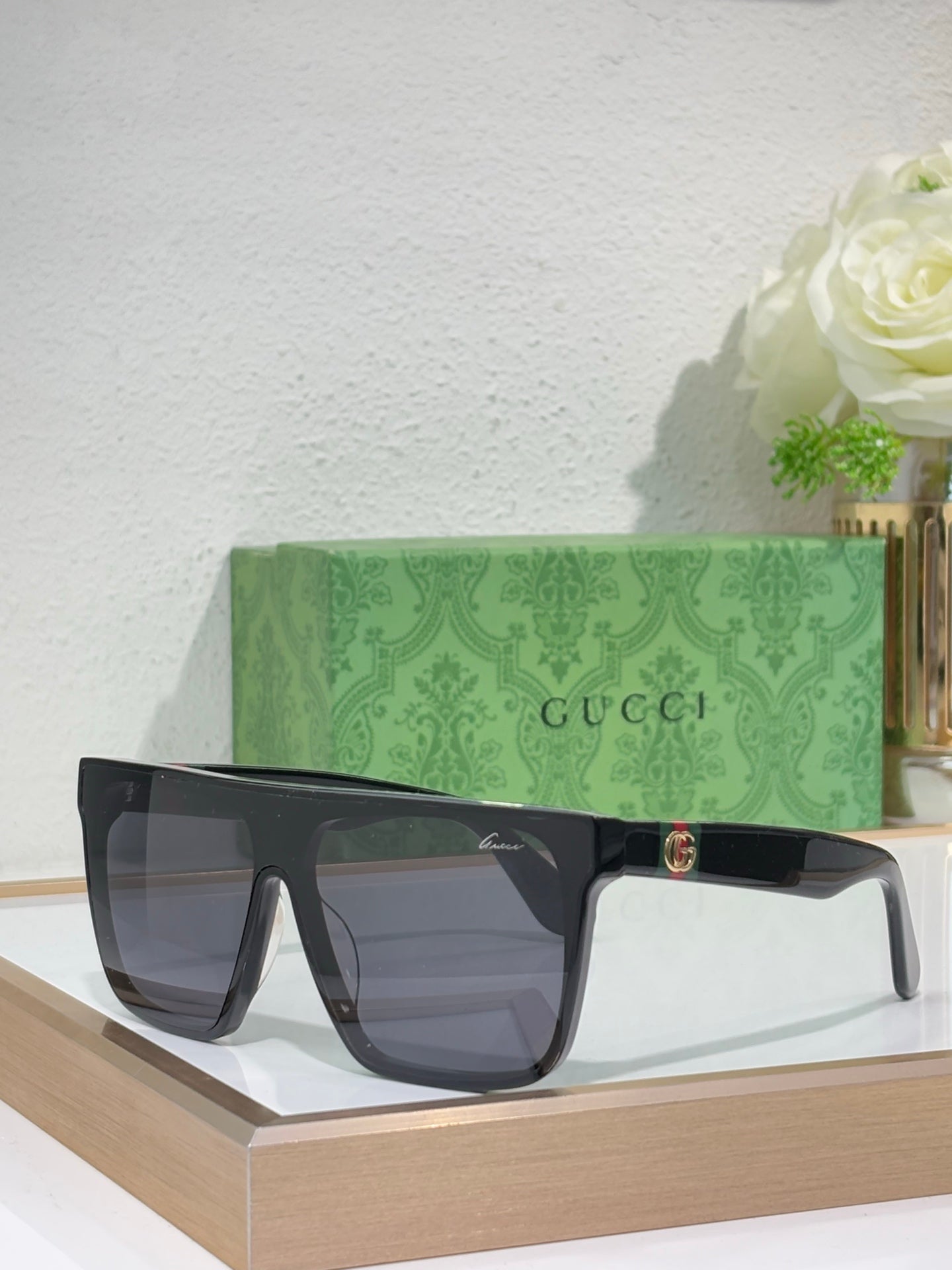 Gucci sunglasses with black frames and dark gray lenses, gold emblem at center