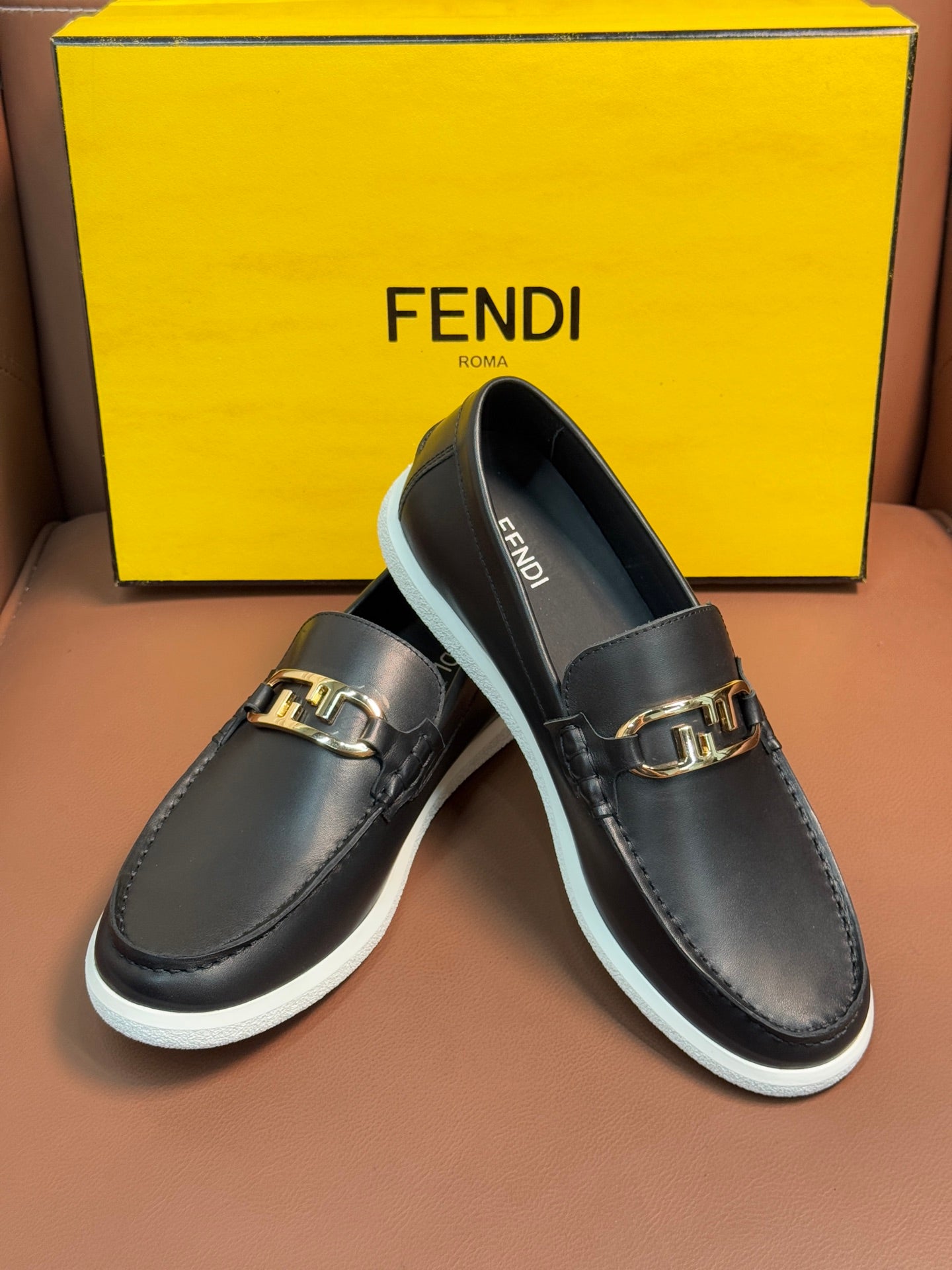 Fendi unisex loafers in dark leather with gold buckle, white rubber soles, angled view