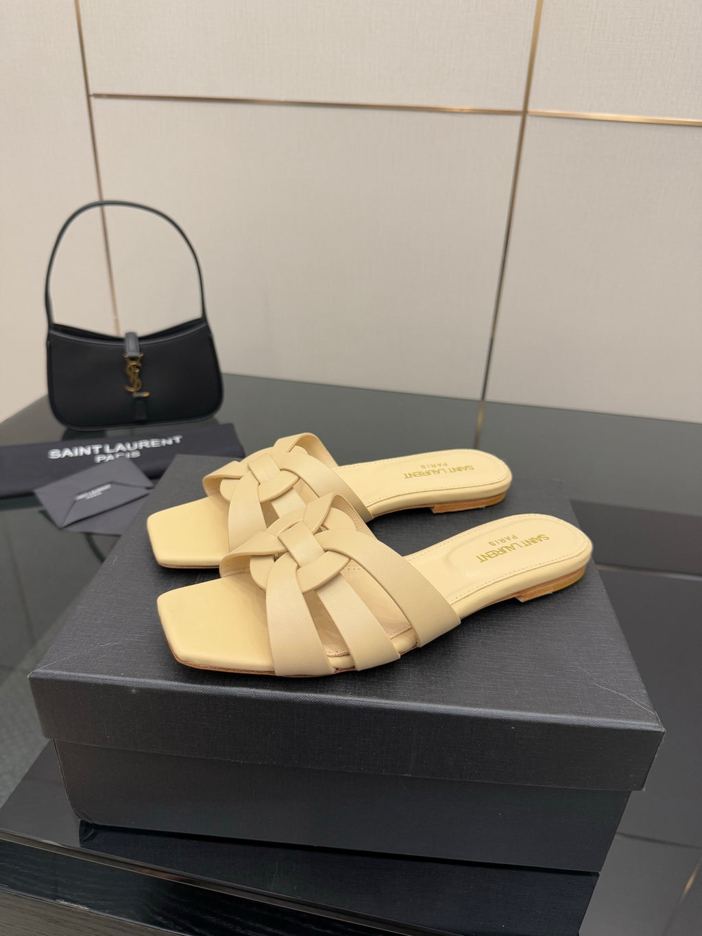 Women’s beige slide sandals with braided cross straps on black box display