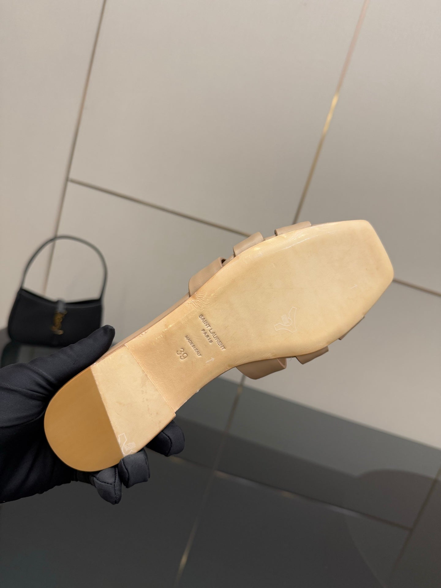 Beige flat sandal outsole held by a gloved hand, minimal tread