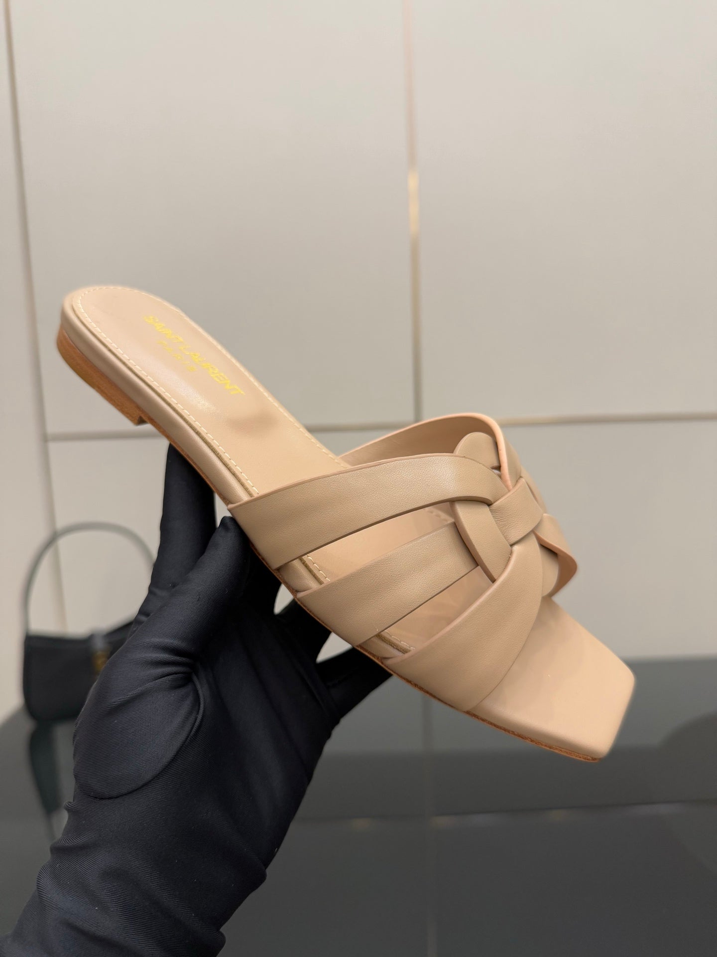 Beige woven-strap slide sandal with open toe, held up for close-up