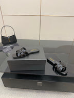 Black slide sandals on a box, patent straps with metallic buckle and shine trim