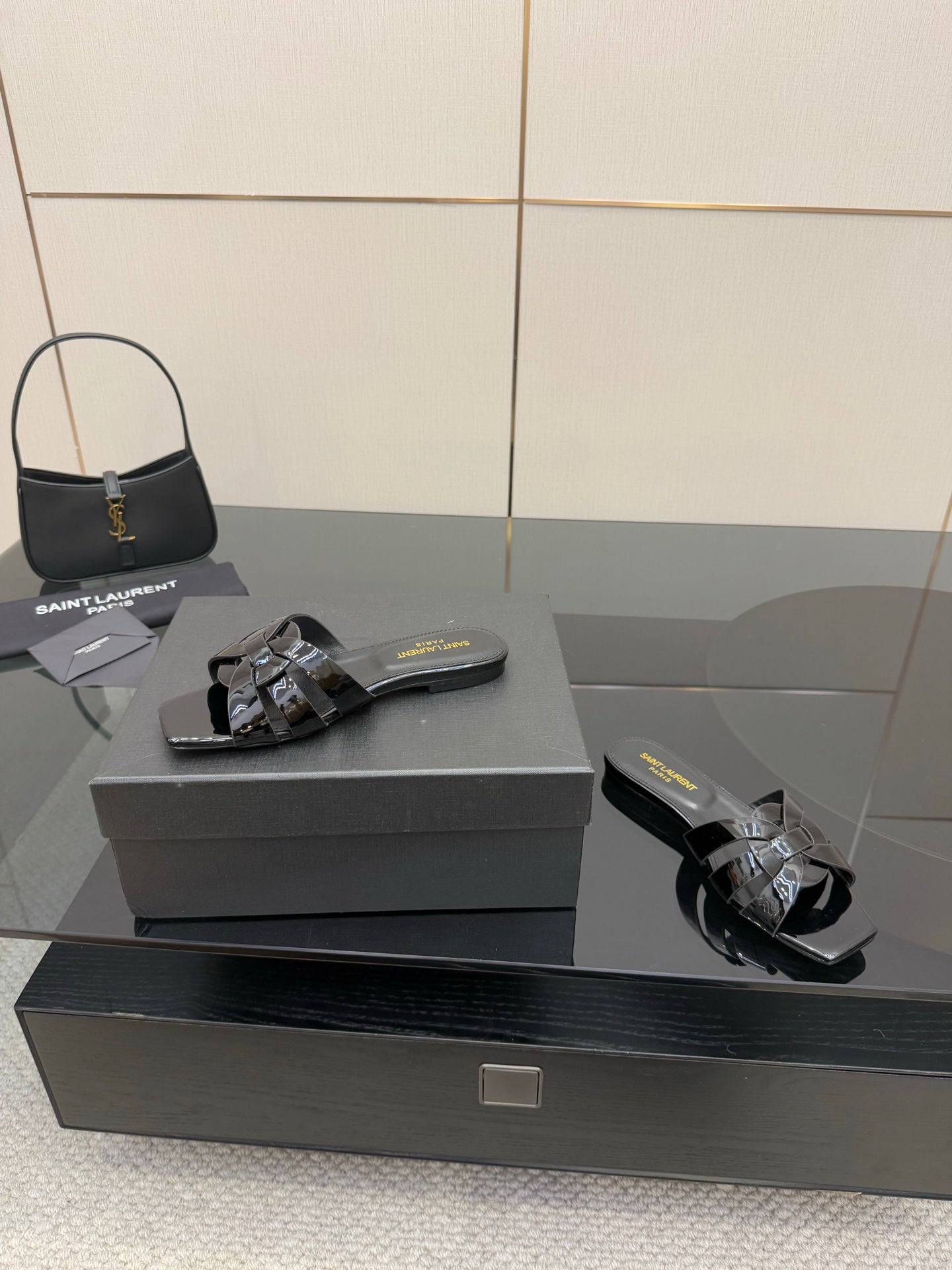 Black slide sandals on a box, patent straps with metallic buckle and shine trim