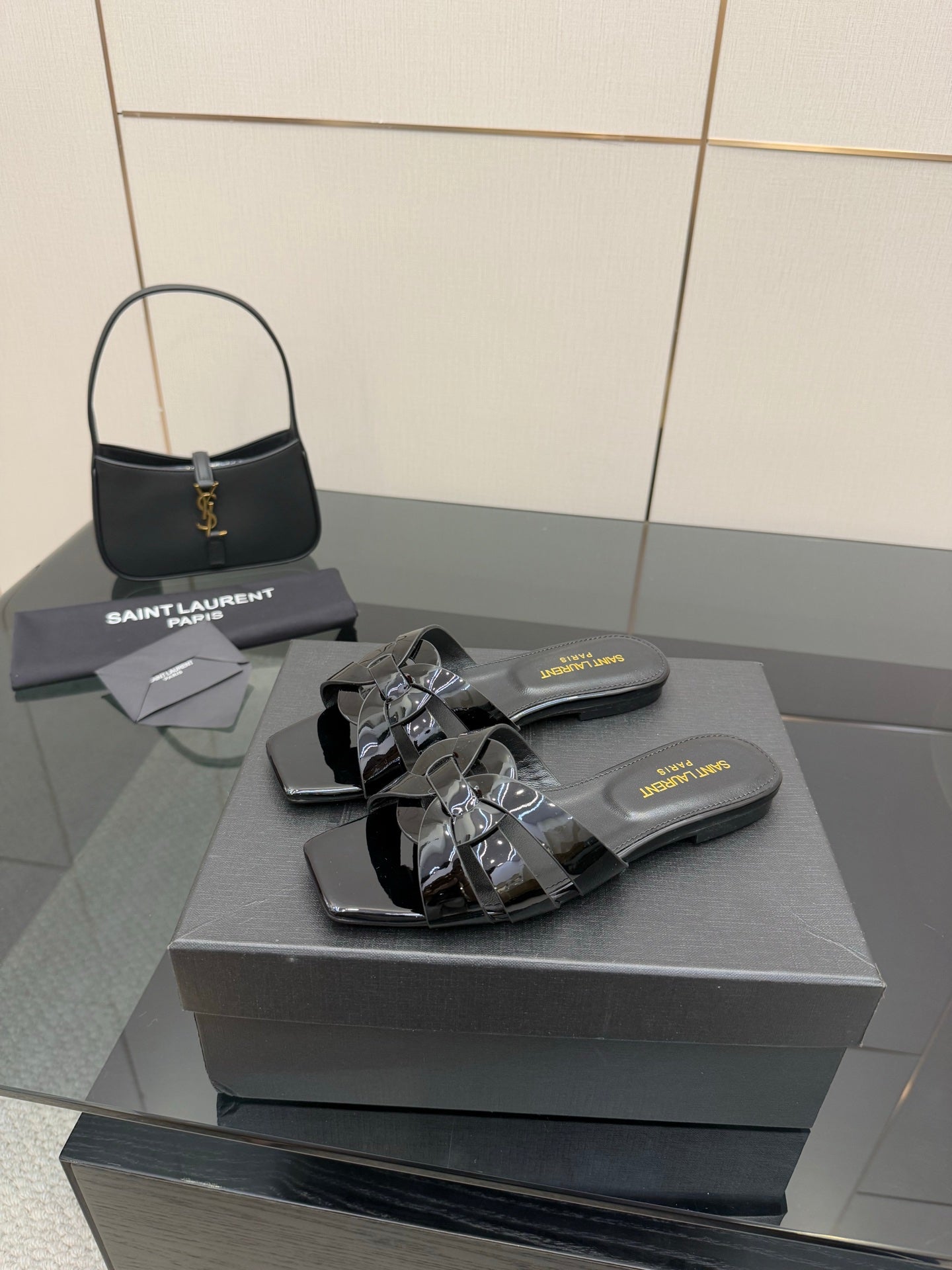 Black slide sandals with patent bow-like strap accents and metallic buckle hardware