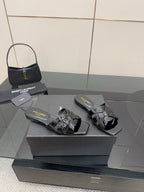 Black slide sandals on a box, patent straps with metallic buckle and shine detail