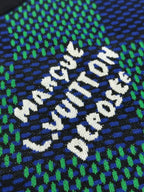 Close-up of white embroidered text on blue and green checkerboard knit