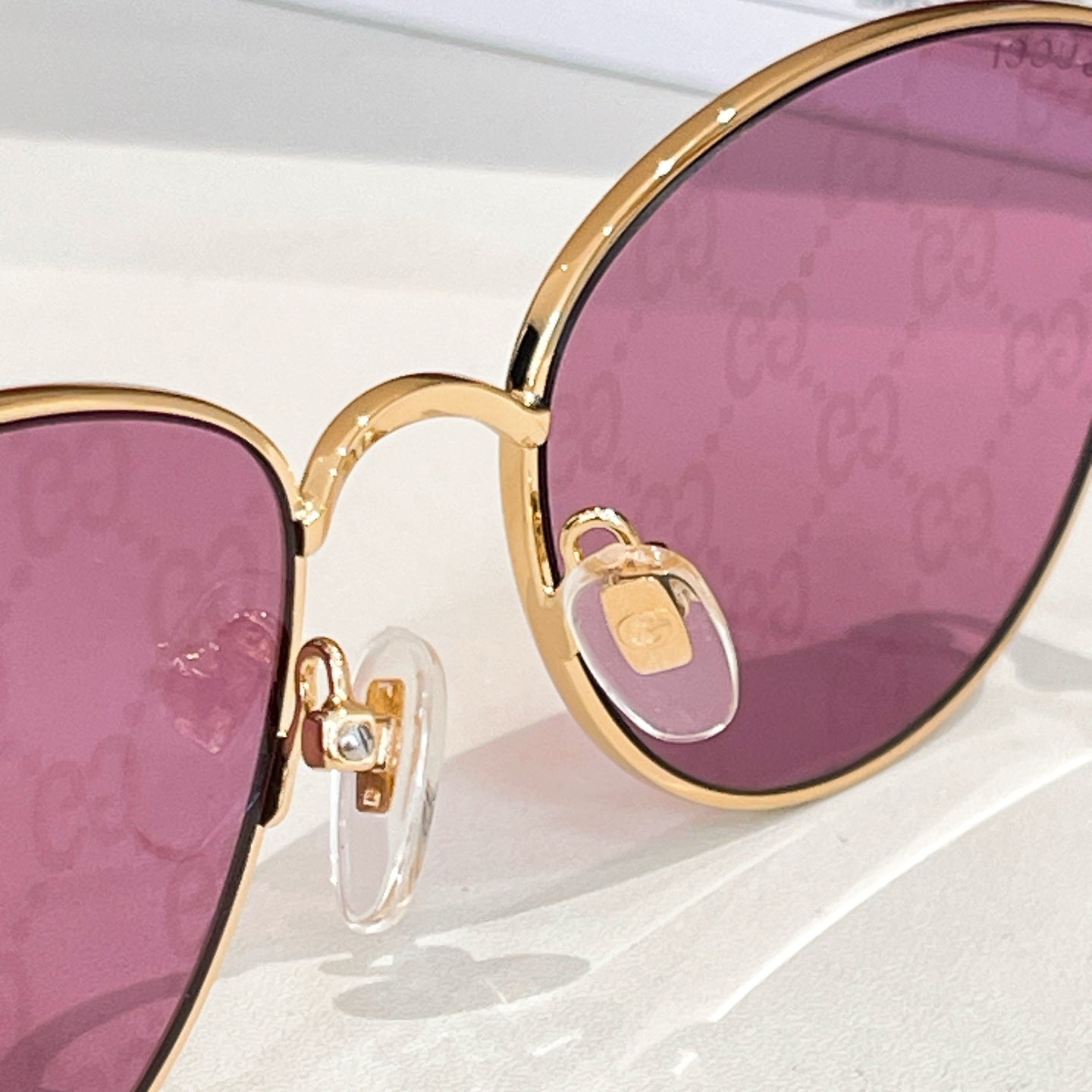 Sunglasses close-up: gold frame with purple GG-pattern lenses.