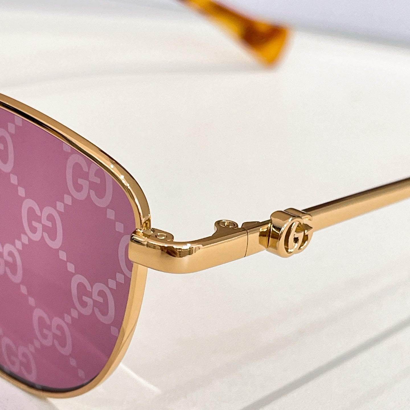 Sunglasses close-up: gold temple with hinge detail and logo.